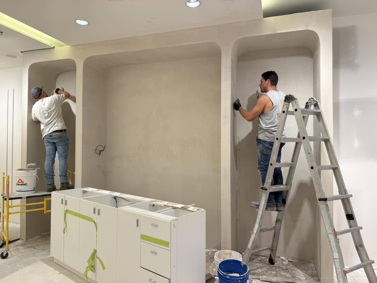 Deux poseurs appliquent un enduit à la truelle sur des niches murales arrondies