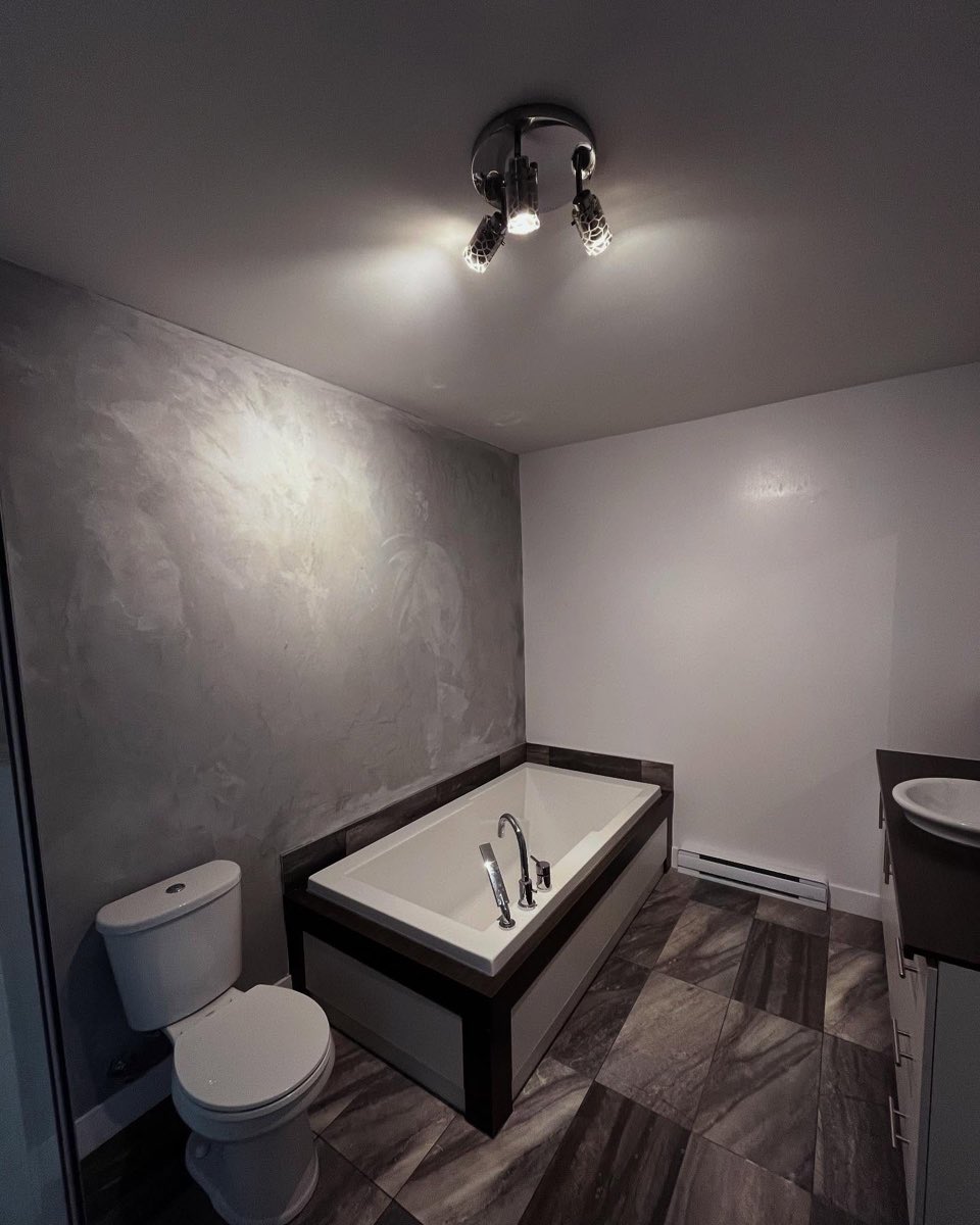 Salle de bain avec mur en enduit décoratif gris nuagé autour d'un bain encastré