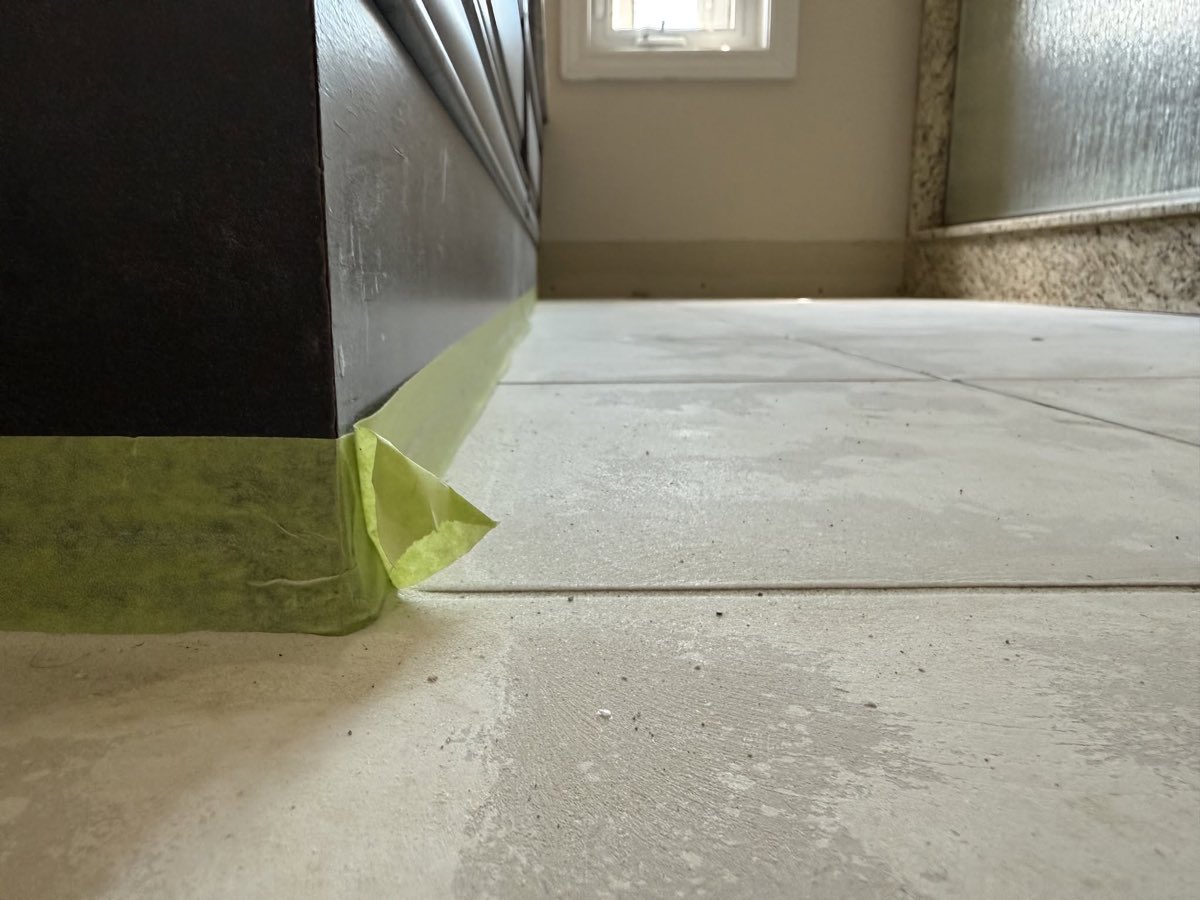 Avant l'application, ancien plancher de céramique rubané au pied d'une vanité foncée, joints de carrelage encore visibles