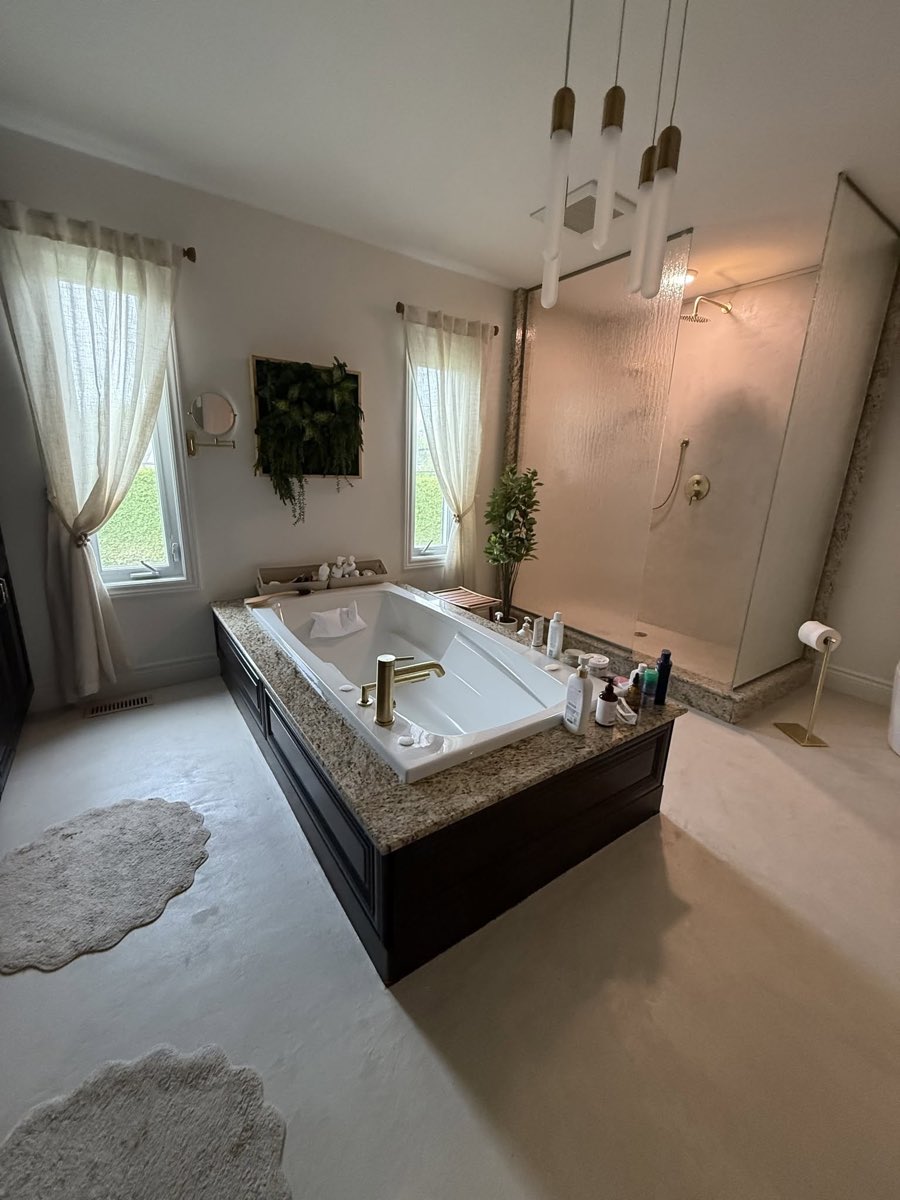 Salle de bain terminée, plancher de microbéton clair sans joint et bain encastré dont le dessus est en granit