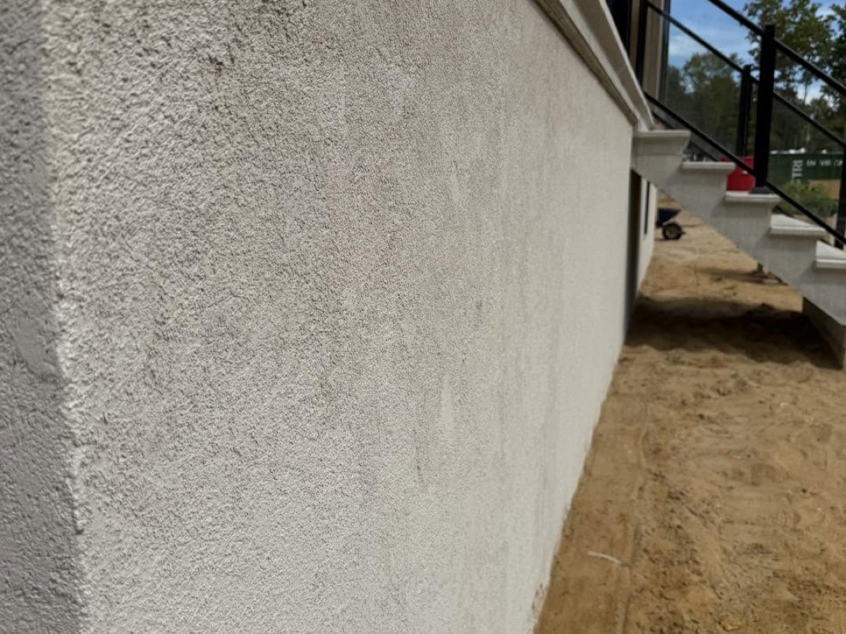 Mur de fondation après crépi, fini texturé gris clair et arête nette en haut du solage