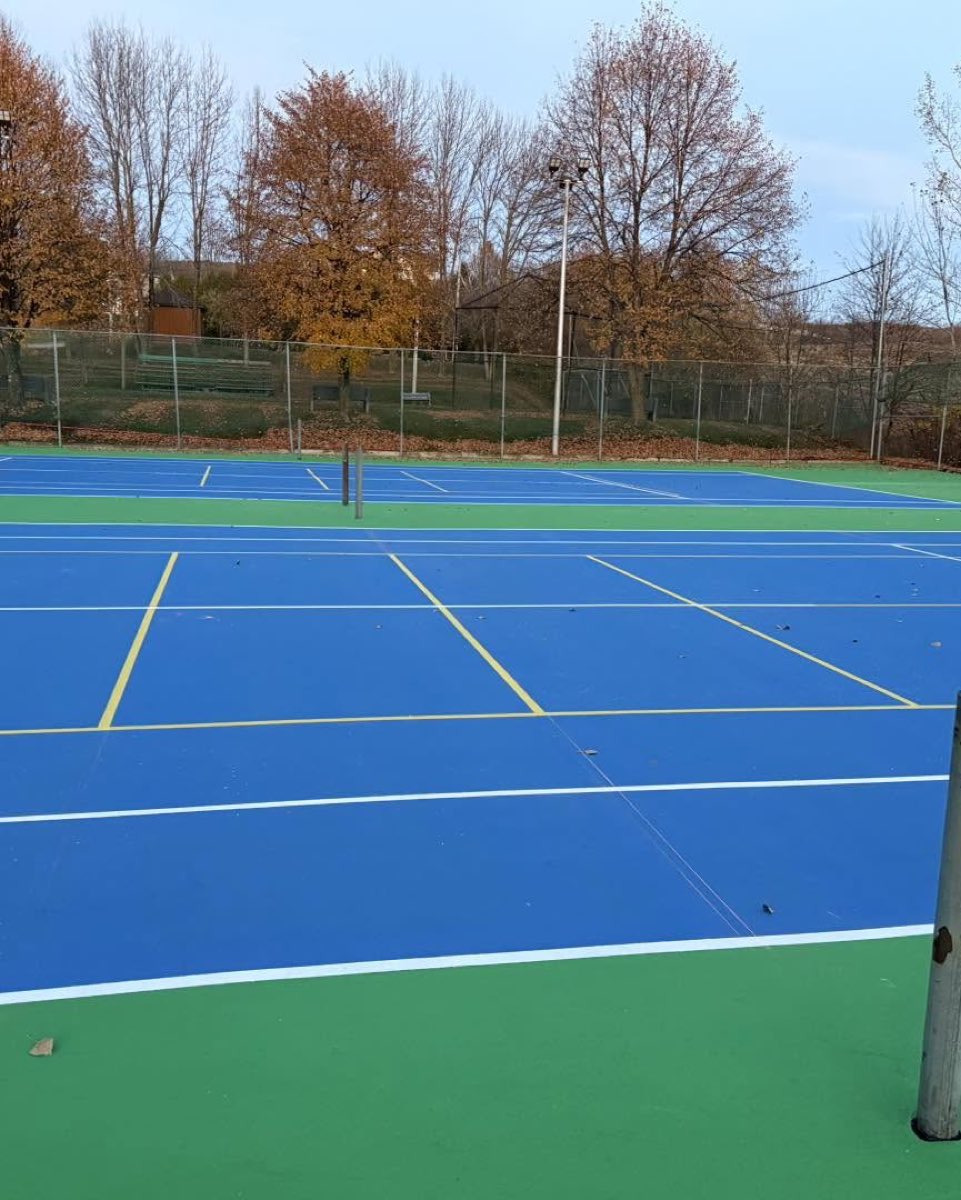 Terrain de tennis à surface acrylique avec lignage jaune, arbres d'automne à l'arrière